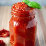 Overfilled jar of fresh tomato sauce topped with fresh basil