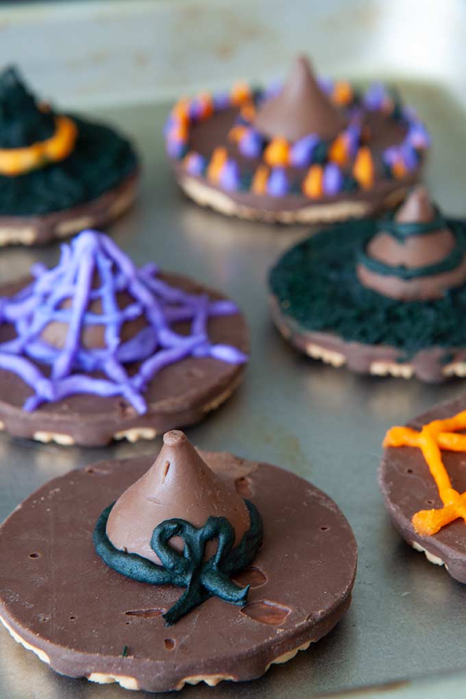 A tray of cookie witch hats, all decorated with black, purple, and orange frosting