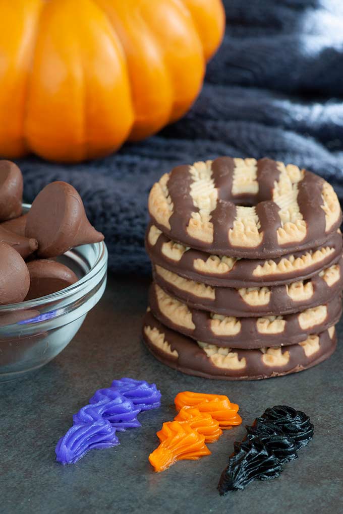 Stack of fudge stripe cookies, bowl of chocolate kisses and smudges of purple, orange, and black frosting