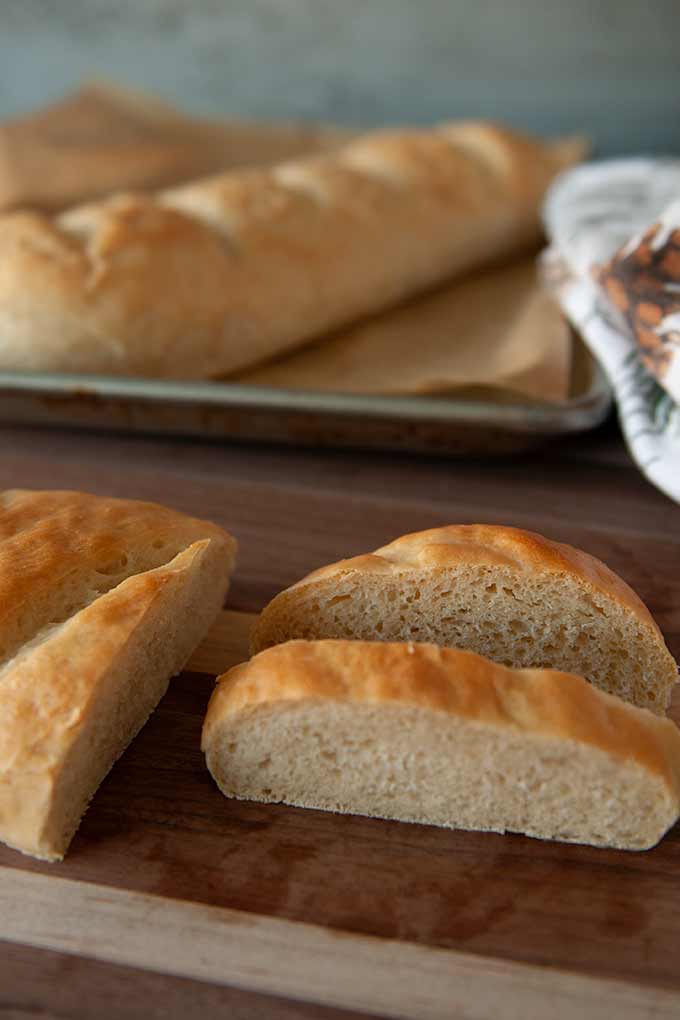 Two loaves of baked homemade French Bread, one is cut into slices
