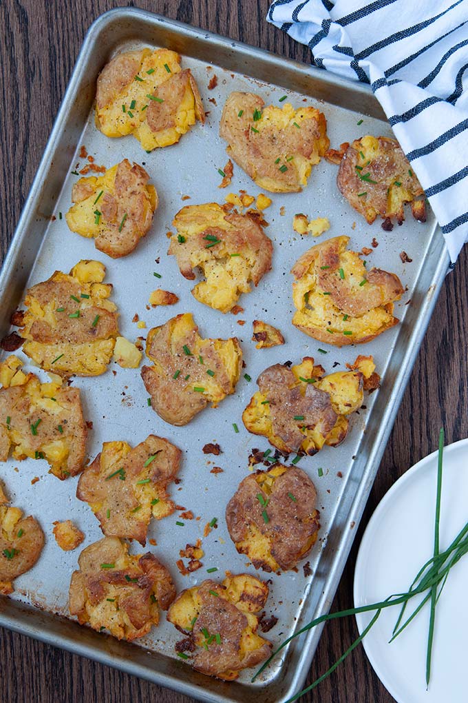 Salt and vinegar smashed potatoes on baking sheet topped with chives, salt and pepper