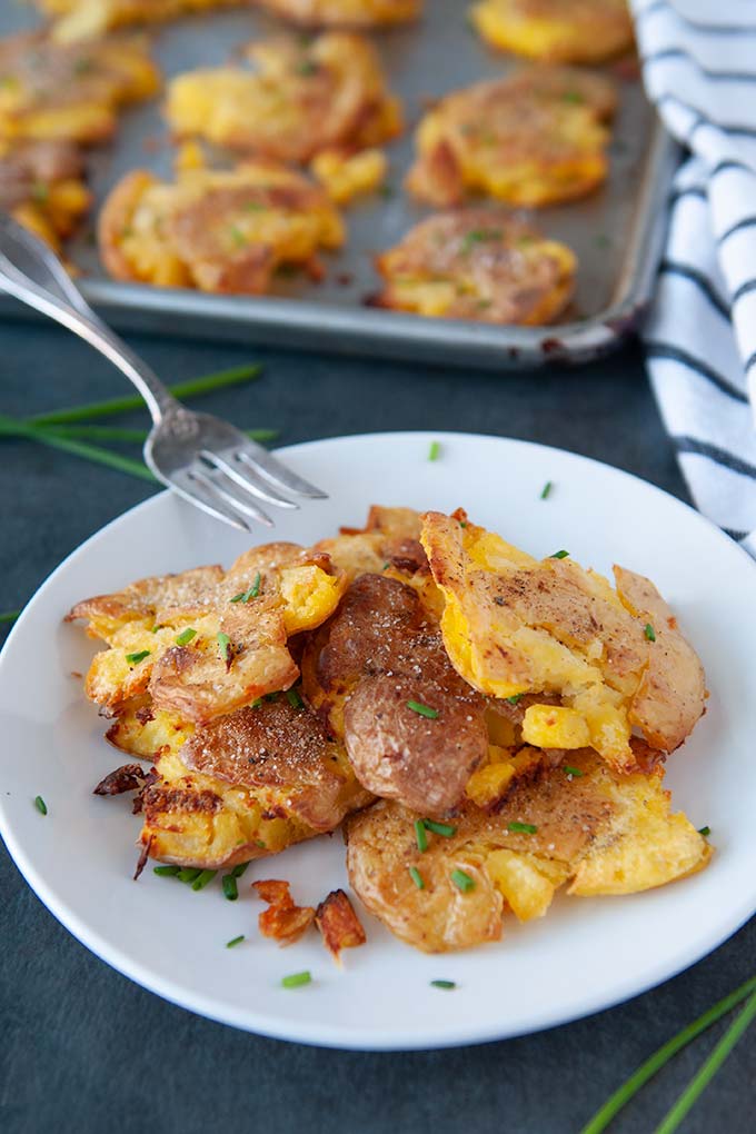 Salt and vinegar smashed potatoes on a plate topped with chives, salt and pepper