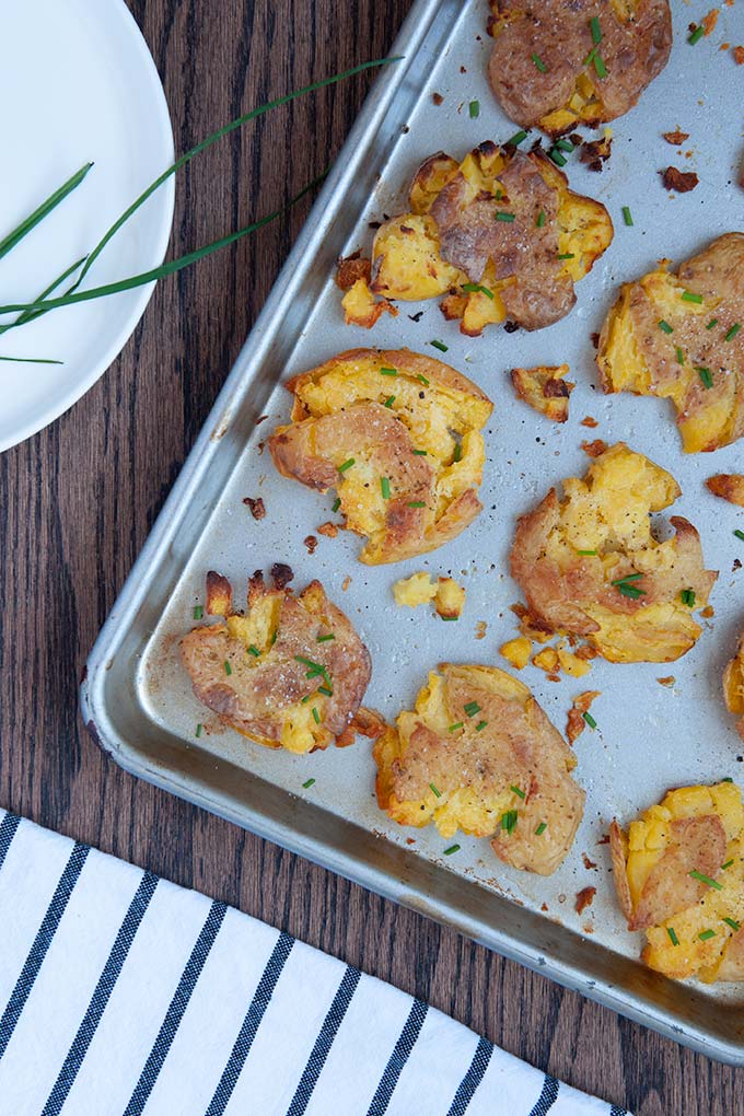 Salt and vinegar smashed potatoes on baking sheet topped with chives, salt and pepper