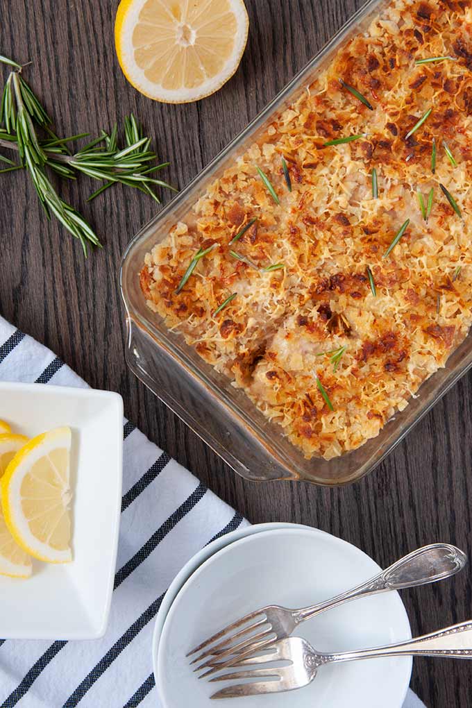 Tuna casserole with potato chips in baking dish with lemon slices, bowls, and utensils