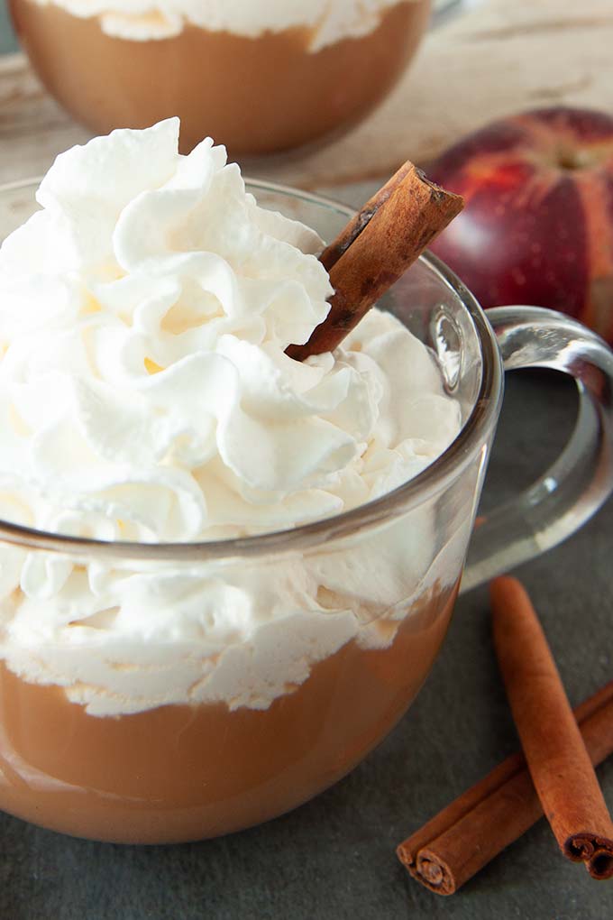 A close up of a mug of apple cider cocktail topped with whipped cream and a cinnamon stick