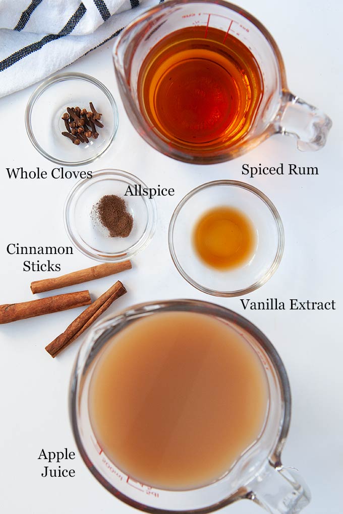All of the ingredients needed to make the apple cider cocktail such as apple juice, spiced rum, and spices.