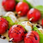 Up close of tomatoes, basil, and mozzarella balls on skewers drizzled with balsamic glaze and sprinkled with salt and pepper