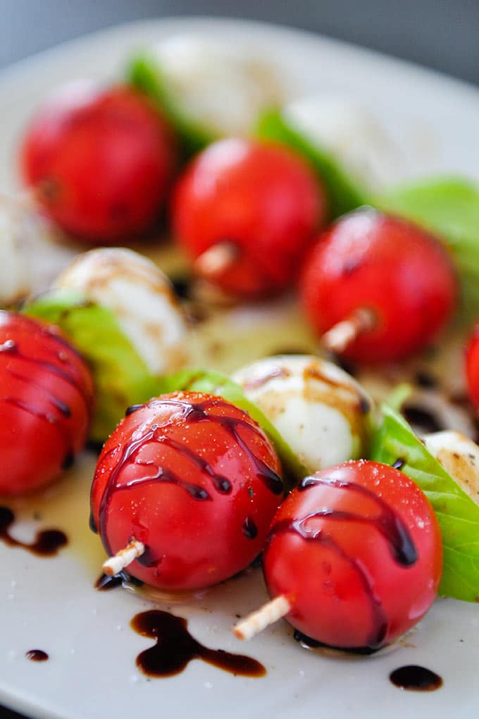 Up close of tomatoes, basil, and mozzarella balls on skewers drizzled with balsamic glaze and sprinkled with salt and pepper
