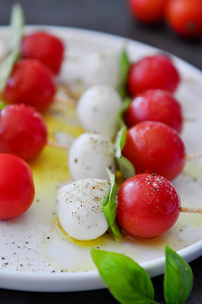 Up close of caprese salad skewers drizzled with olive oil, salt, and pepper on a white plate