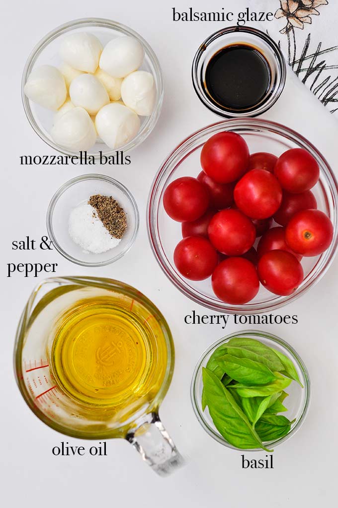All ingredients needed to make caprese salad skewers such as cherry tomatoes, mozzarella balls, and a really good olive oil