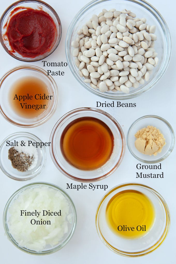 All of the ingredients to make baked beans such as finely diced onion, dried great northern beans, maple syrup and tomato paste.