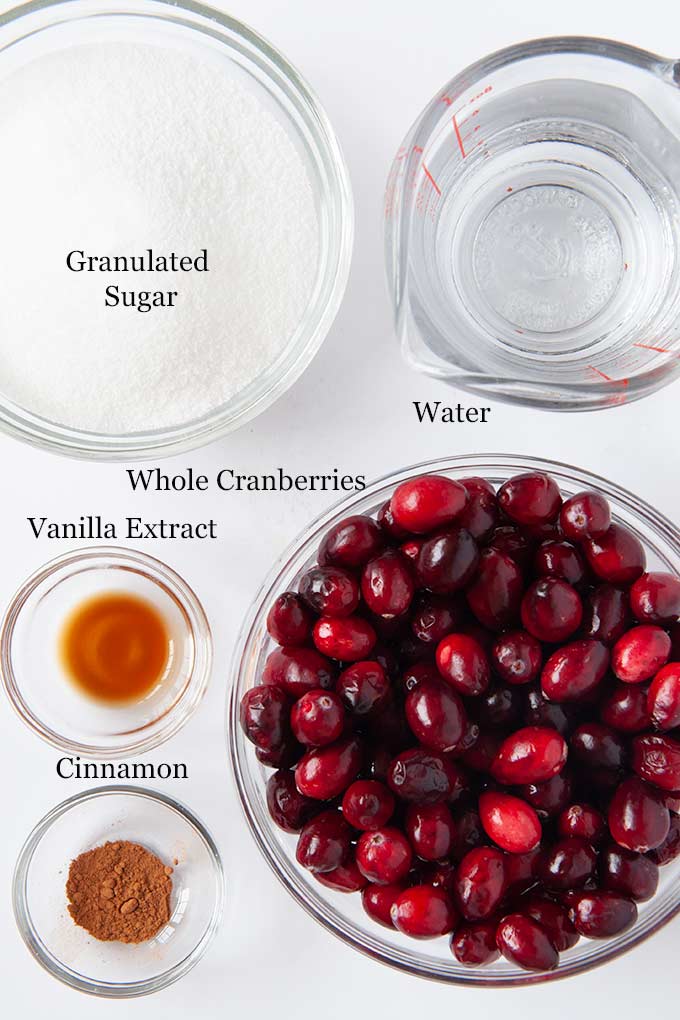 All of the ingredients to make cranberry sauce like granulated sugar, fresh cranberries, vanilla extract, and cinnamon.