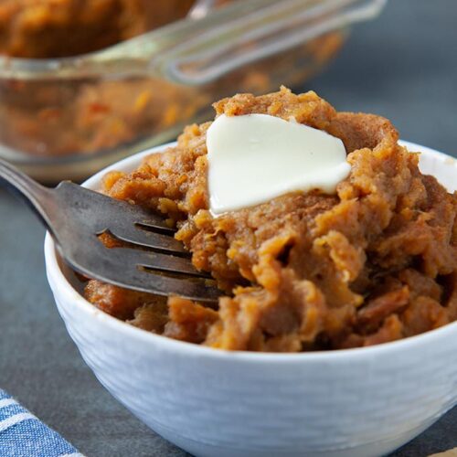 A fork in a bowl of mashed sweet potatoes topped with a pat of margarine