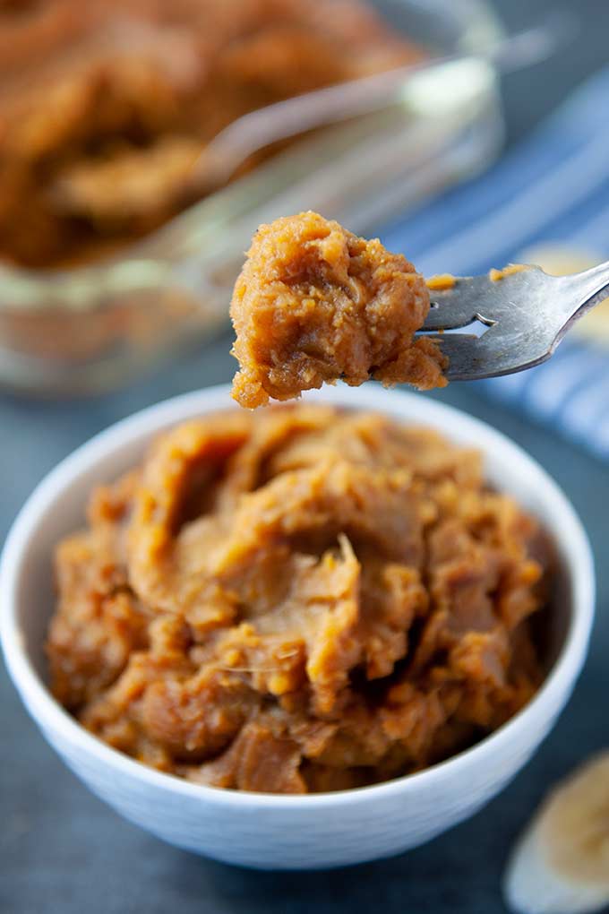 A forkful of mashed sweet potatoes above the bowl which is blurred in the background“> 