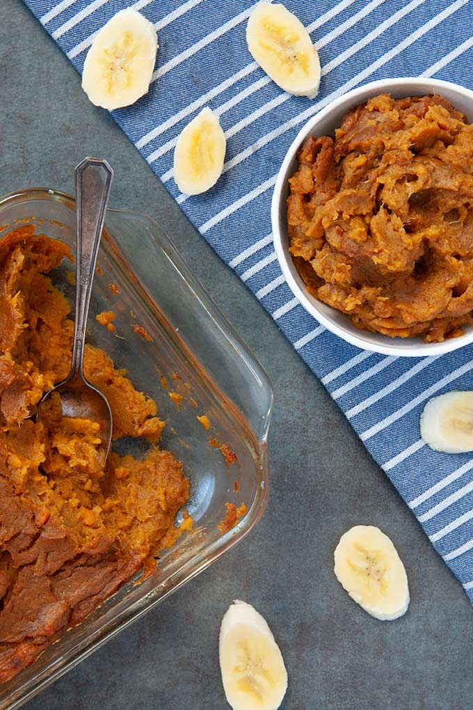 A baking dish full of healthy mashed sweet potatoes, a bowl of mashed sweet potatoes with banana slices sprinkled around“> 