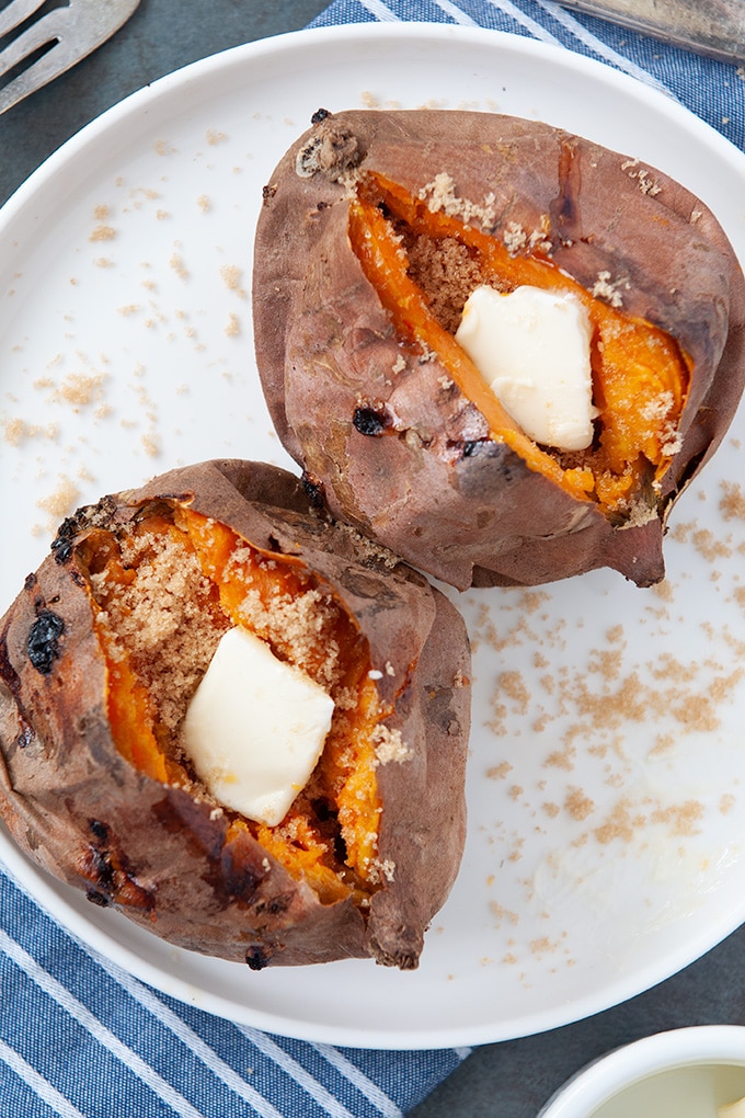 Two sweet potatoes topped with butter, brown sugar, and cinnamon on a white plate.