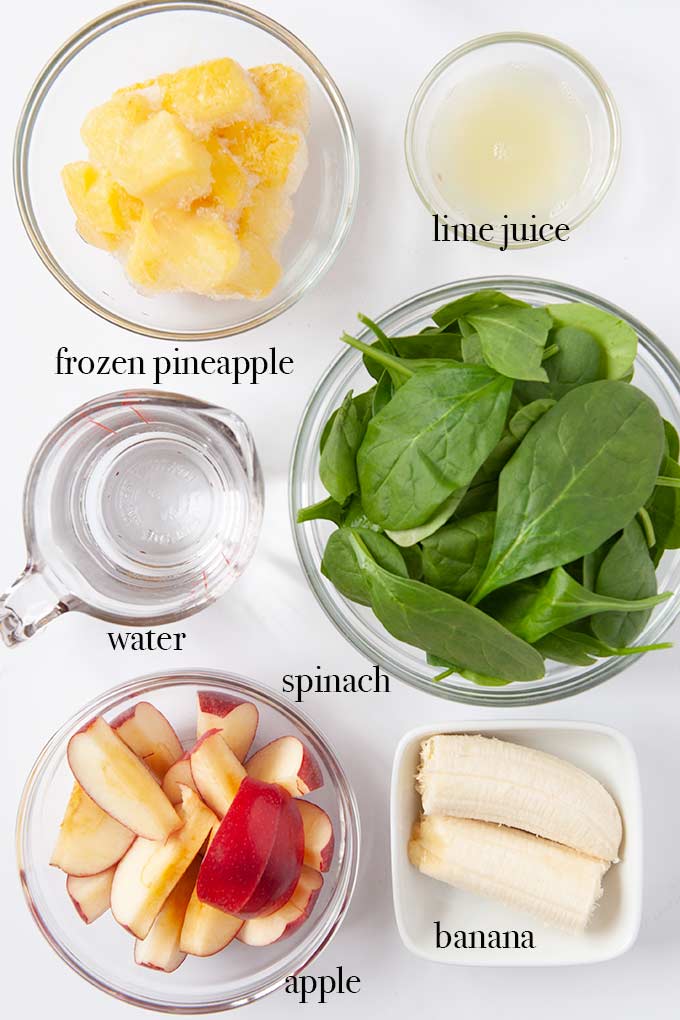 All of the ingredients needs to make green smoothies like apples, spinach, lime juice and frozen pineapple.