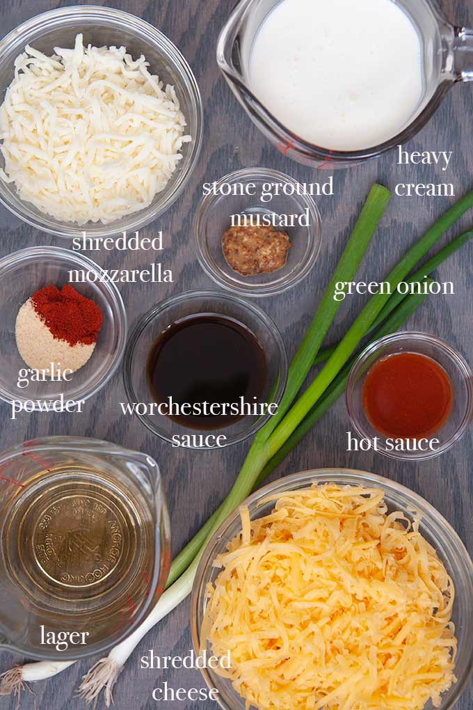 All of the ingredients needed to make beer cheese dip such as shredded cheese, lager, stone ground mustard, and heavy cream.