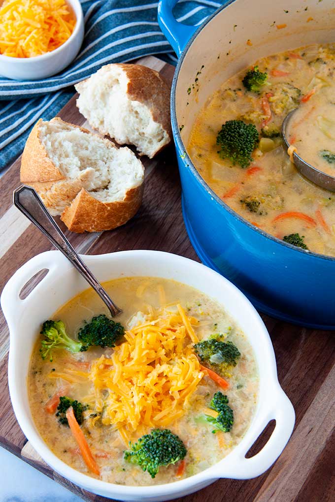 A white bowl full of soup topped with cheese, a blue pot full of soup in background with torn bread.