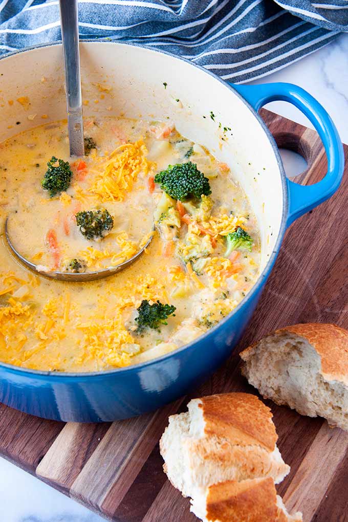 Pot full of broccoli cheese soup with a ladle and bread.