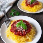 Two plates of spaghetti squash topped with fresh tomato sauce, parmesan cheese, and fresh basil.
