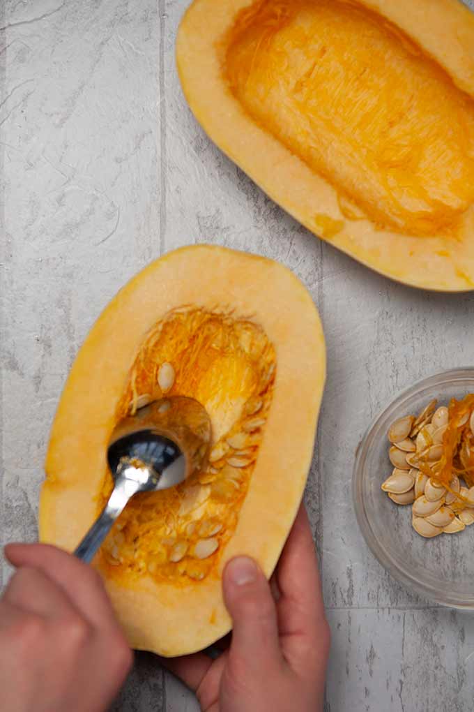 Scooping out squash seeds with a spoon from a cut in half spaghetti squash