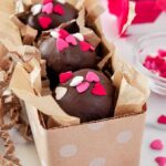 Up close of three Nutella truffles covered in pink, white, and red heart-shaped sprinkles in a small rectangular polka dot box