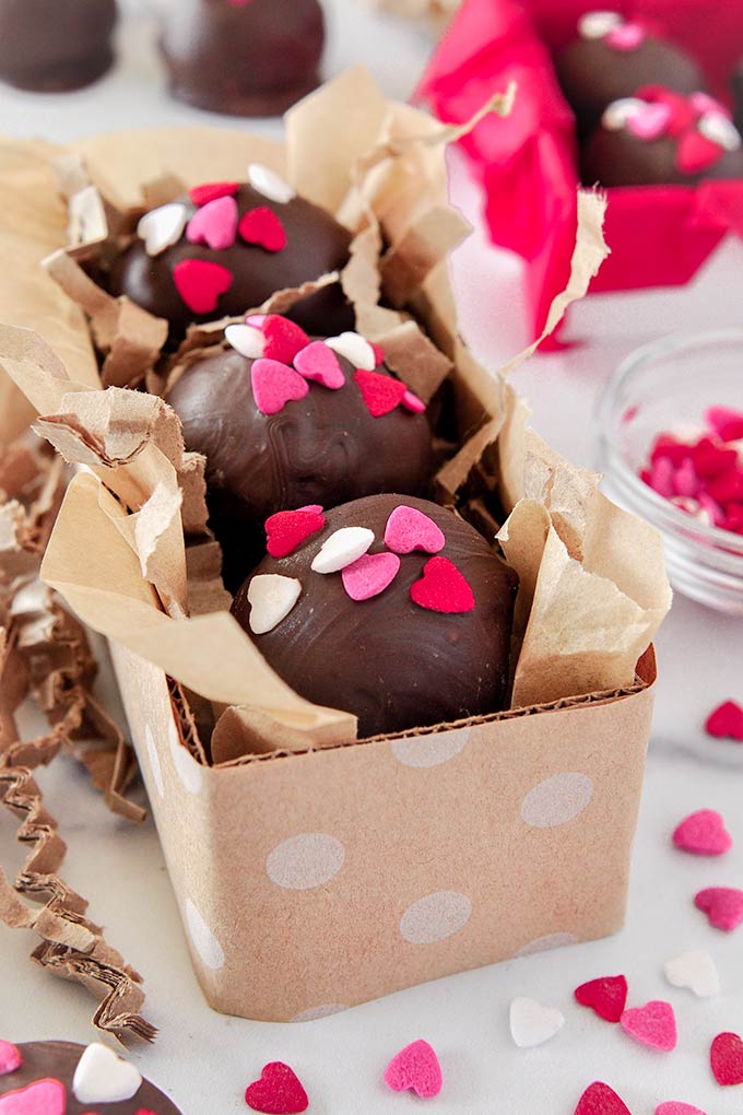 Up close of three Nutella truffles covered in pink, white, and red heart-shaped sprinkles in a small rectangular polka dot box