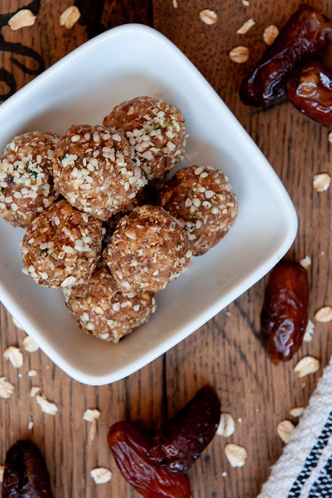 Energy balls in a small square bowl, wooden background with whole dates and oats.