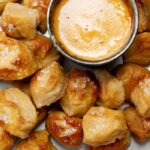 Up close salted pretzel bites with metal cup of hot beer cheese dip