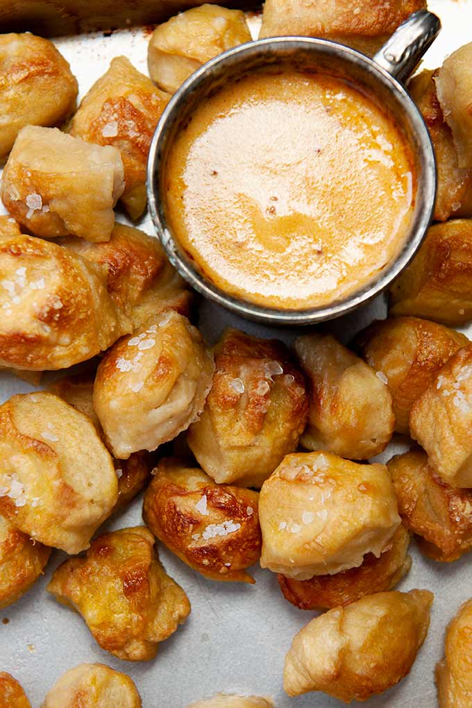 Up close salted pretzel bites with metal cup of hot beer cheese dip