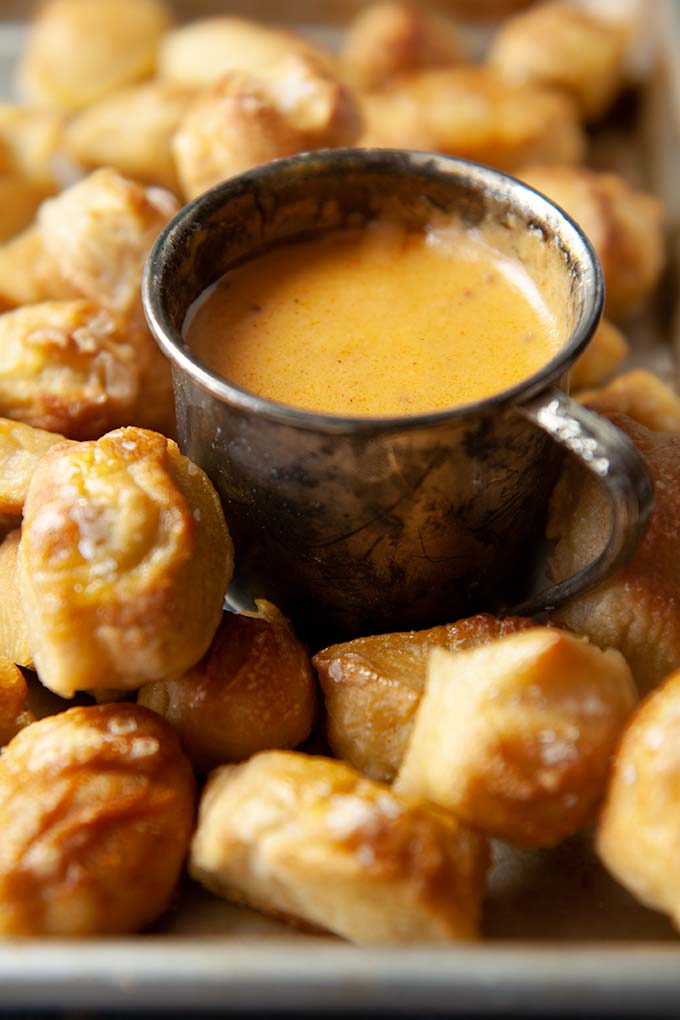 Up close salted pretzel bites with metal cup of hot beer cheese dip
