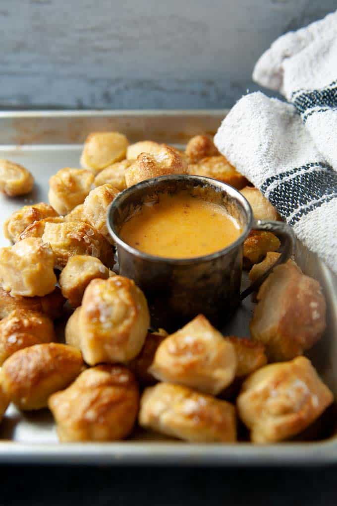 Up close salted pretzel bites with metal cup of hot beer cheese dip