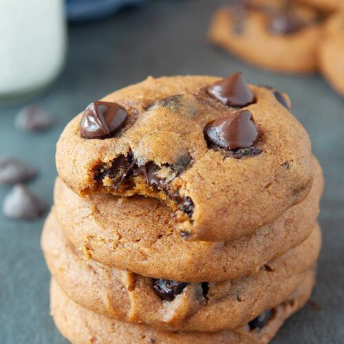 Stack of pumpkin chocolate chip cookies with bite taken out of top cookie and glass of cold milk