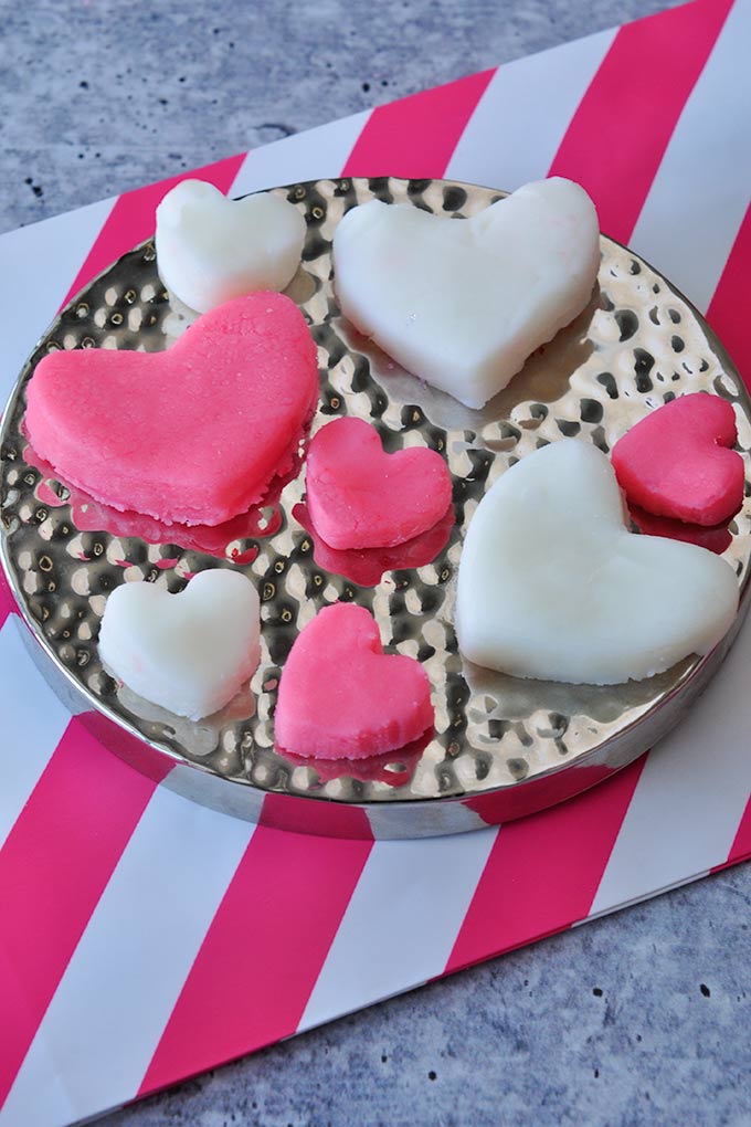 Pink and white Valentine candy hearts in small and big sizes on a silver tray on a pink and white striped background