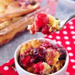 A big spoonful of cherry dump cake above a white bowl and the baking dish in the background.