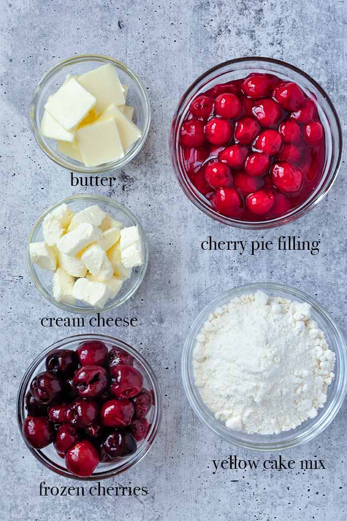 All of the ingredients to make cherry dump cake such like cherries, cake mix, cream cheese, and butter.