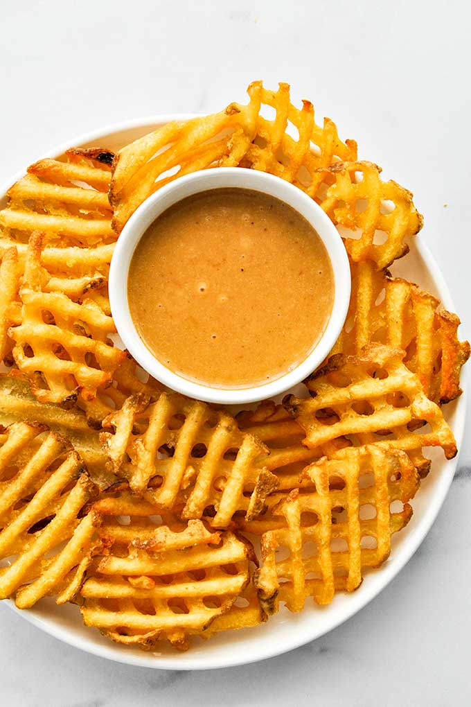 A small white bowl of Chick-fil-A sauce with waffle fries all around.