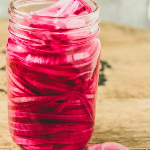 A close up of a large jar full of red onions with some onions by the jar.