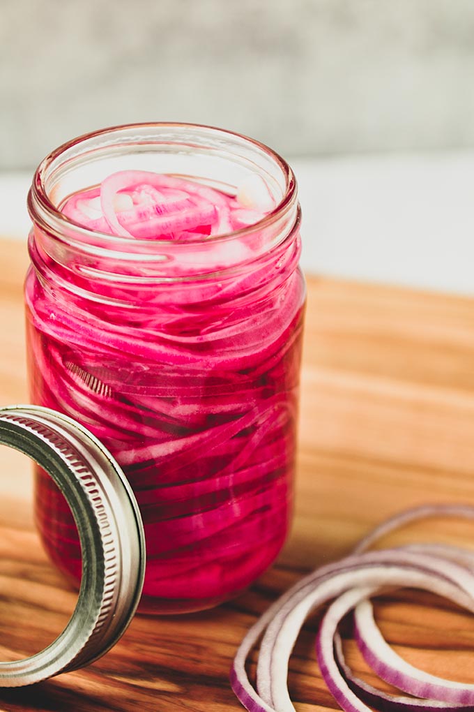 A close up of a large jar full of red onions with some onions by the jar.