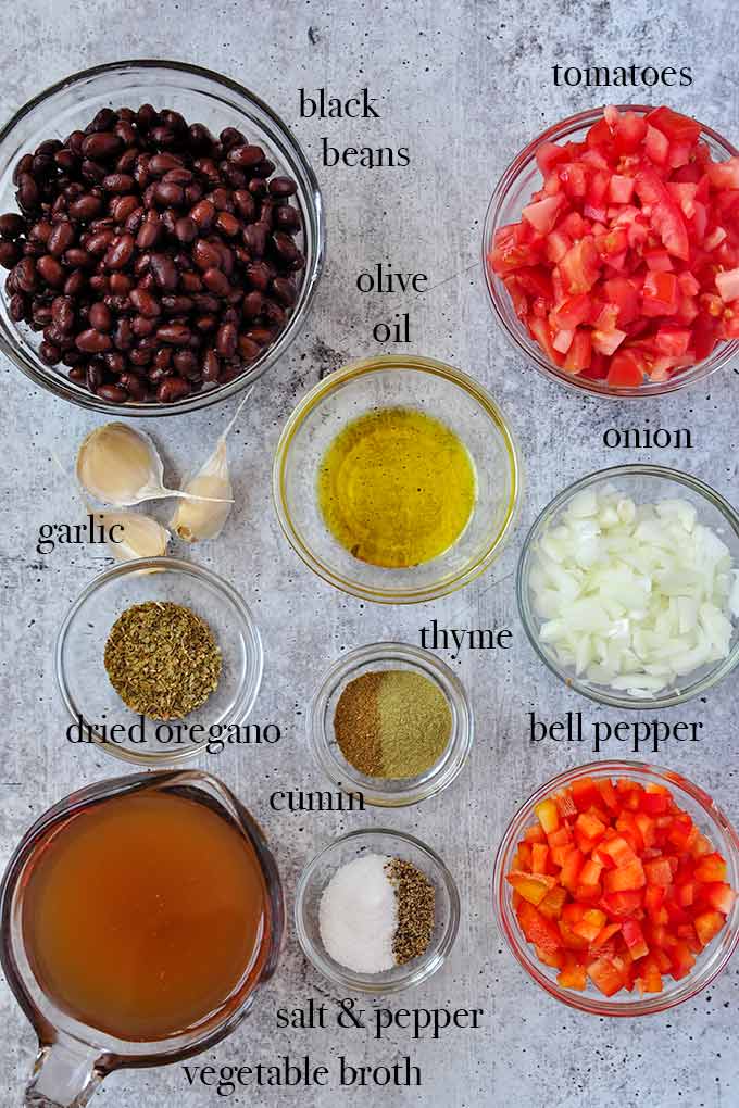 All of the ingredients needed to make black bean soup such as black beans,  tomatoes, bell pepper, and vegetable broth.