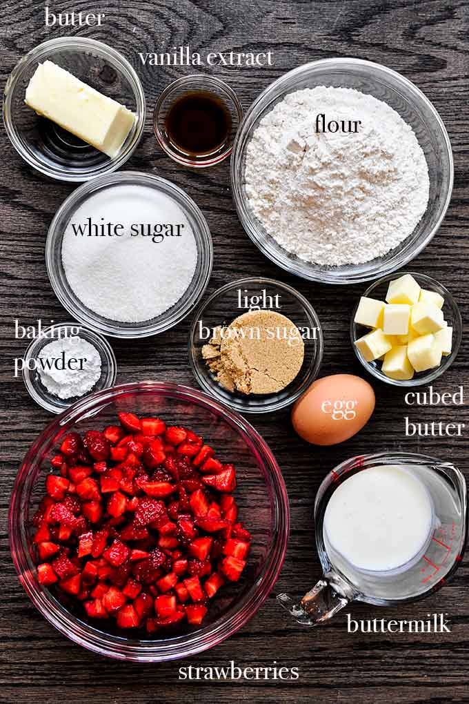All of the ingredients needed to make strawberry muffins such as flour, strawberries, butter, brown sugar and vanilla extract.