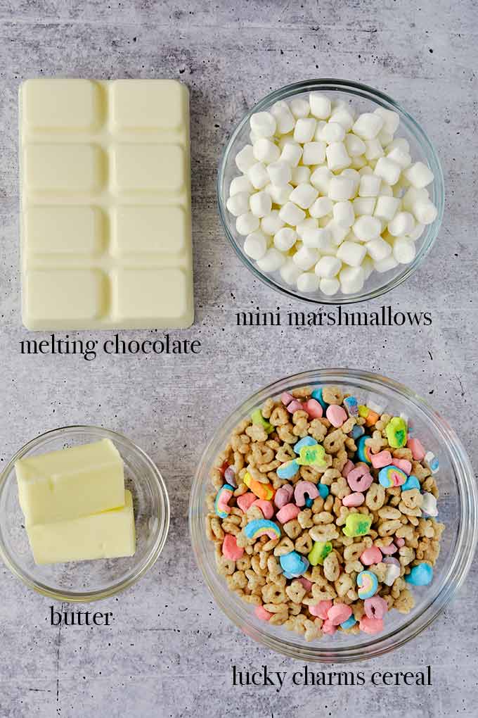 All of the ingredients needed to make marshmallow treats such as mini marshmallows, butter, Lucky Charms, and melting chocolate.