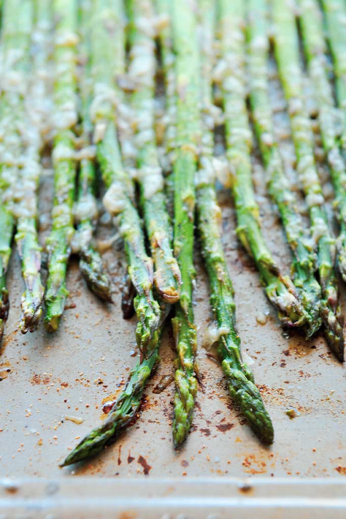 A baking tray with roasted asparagus that are pointed down. 