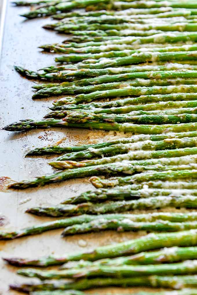 A baking tray with roasted asparagus that is all lined up. 