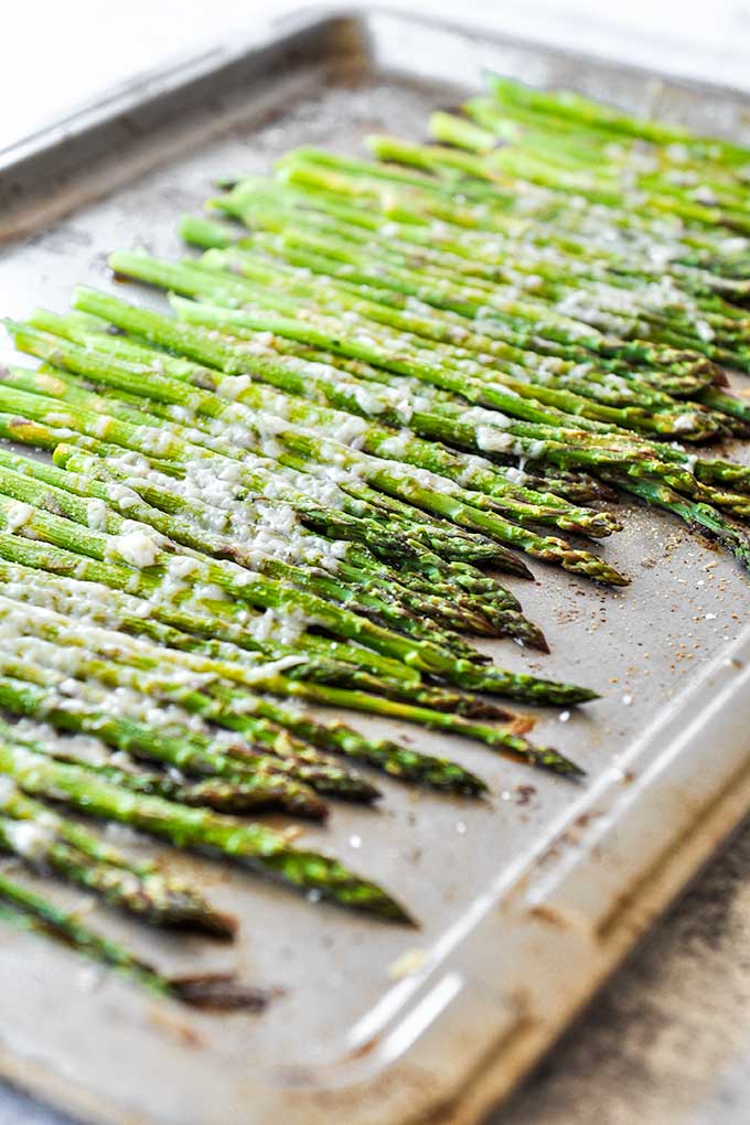A baking tray with roasted asparagus that is all lined up but seen from an angle.