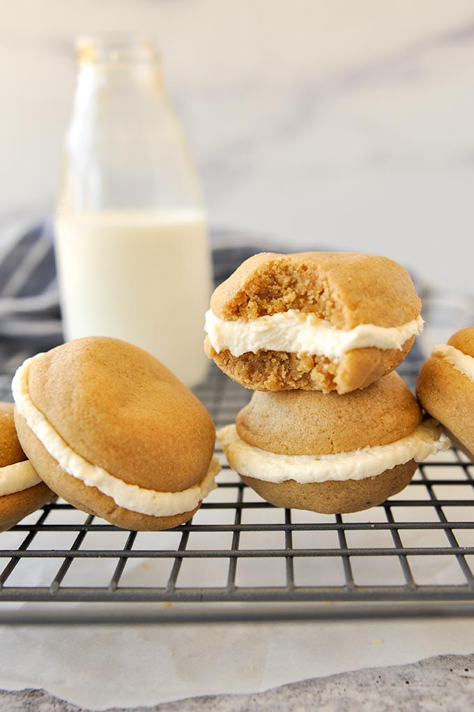 Two stuffed cookies stacked, the top one with a bite missing, and a third cookie is leaning against another on a cooling rack.  Milk bottle in the background.