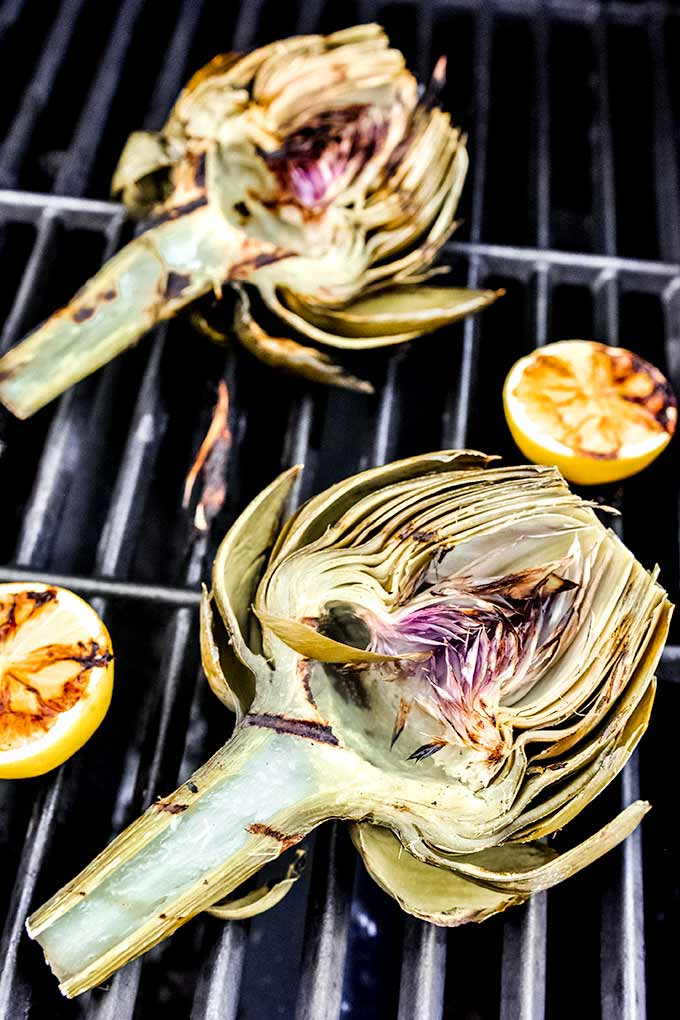 Two halves of artichoke on the grill with grilled lemons.