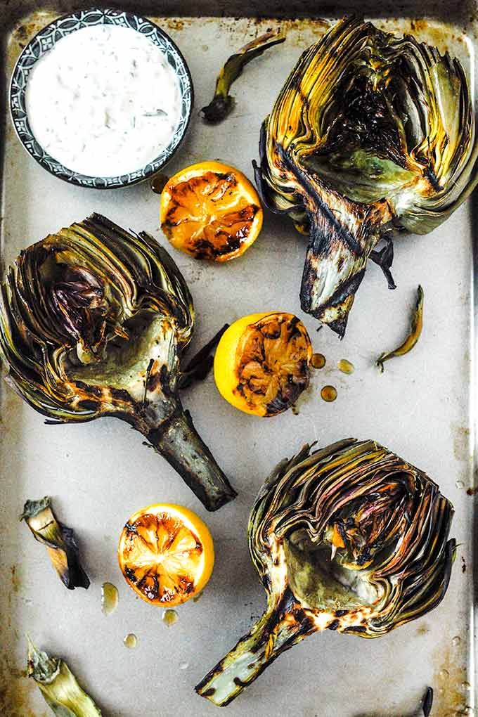 Three halves of artichokes with grilled lemon halves with a small dish of lemon aioli.