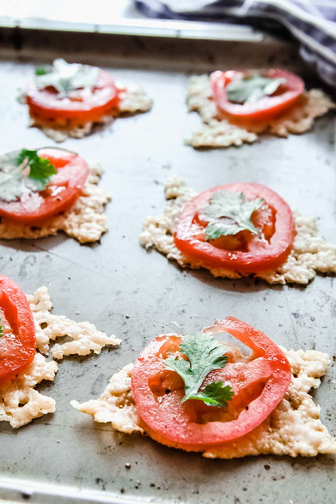 Cheese crisps is as an appetizer topped with a slice of tomato and a leaf of cilantro.